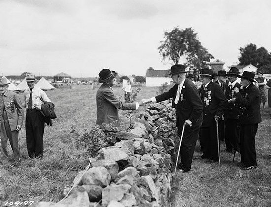 Union and Confederate veterans shake hands across the stone wall at the Angle at Gettysburg during a reunion.