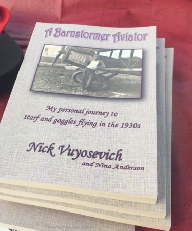 "A Barnstormer Aviator - My personal journey to scarf and goggles flying in the 1930s" a book by Nick Vuyosevich and Nina Anderson. Seen at The Ninety-Nines booth at MMK Fly-in 2018. CB/MDP The book features a black-and-white image of a man standing beside a biplane.