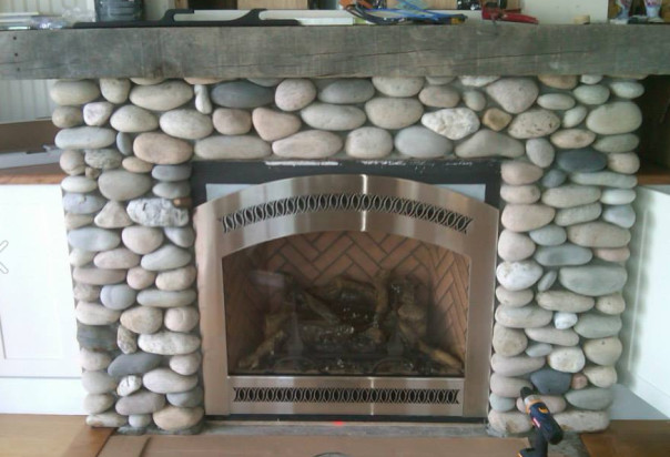 Beach stone fireplace with weathered wood mantel, a custom build example of the work done by Fireworks crew.