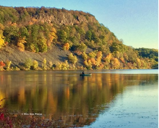 An ancient basalt mountain is mirrored in the waters below with one human in a boat for scale. Photo © Moo Dog Press.